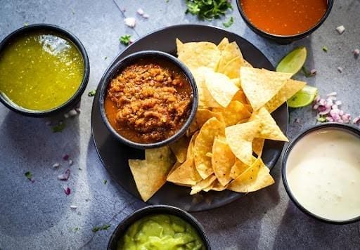 A platter of chips and salsa surrounded by three other dips.